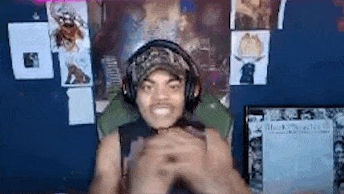 a man wearing headphones and a hat is sitting in a chair in front of a computer .