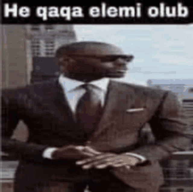 a man in a suit and tie is standing in front of a building with a caption that says he qaqa elemi club .