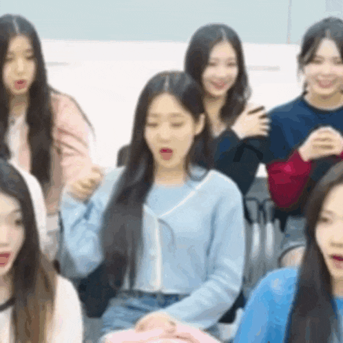 a group of young women are sitting in a room and one of them is wearing a blue sweater .