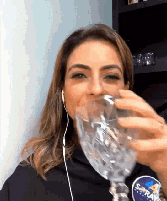 a woman wearing ear buds is drinking from a wine glass