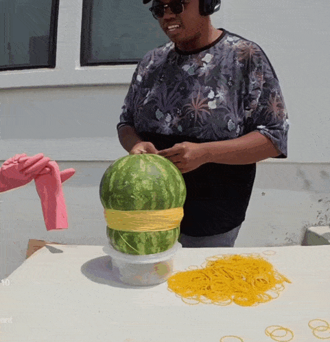 a man in a floral shirt is holding a watermelon with a yellow rubber band around it