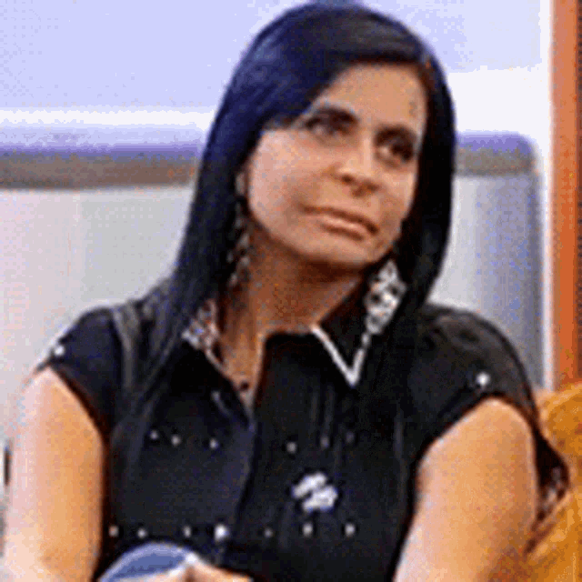a woman with long black hair and earrings is sitting on a couch .
