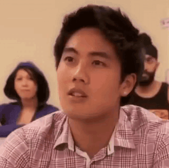 a young man in a plaid shirt is sitting in a classroom .