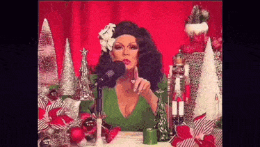 a drag queen is sitting in front of a microphone surrounded by christmas decorations and a nutcracker .