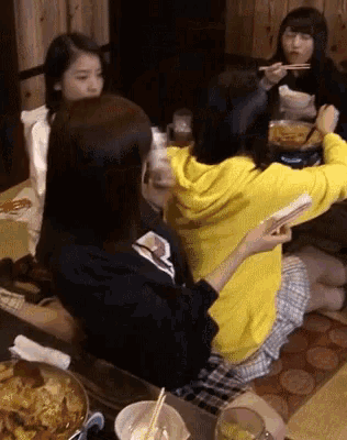 a woman in a yellow hoodie is sitting at a table eating food