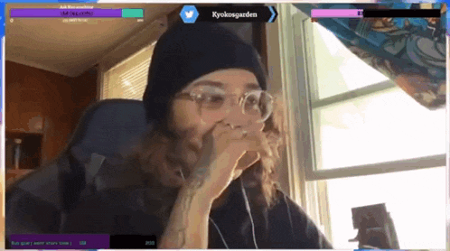 a man wearing glasses and a beanie is sitting in front of a window with the name kyokosgarden on the bottom right