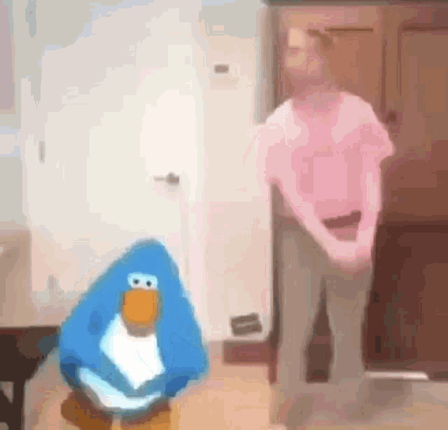 a blue penguin is standing next to a woman in a pink shirt .
