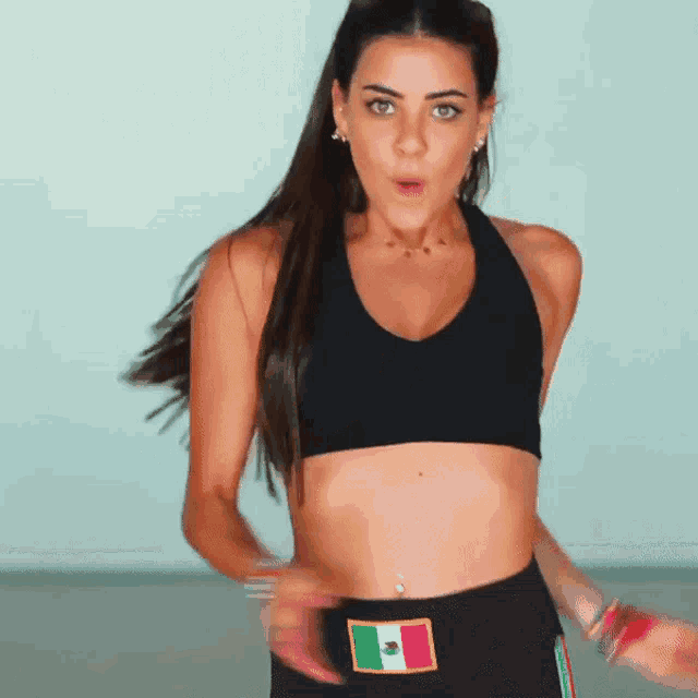a woman wearing a black crop top with a mexican flag patch on her pants