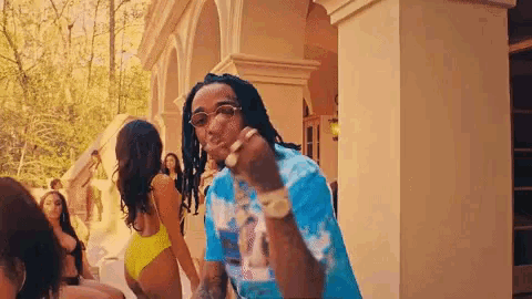 a man in a blue shirt is standing in front of a group of women in swimsuits .