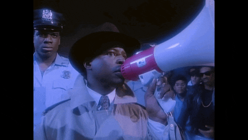 a man in a fedora is holding a megaphone in front of a crowd