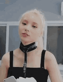 a woman with blonde hair is wearing a black choker and a black tank top .