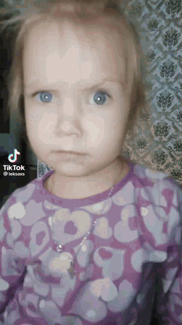 a little girl in a purple shirt is making a funny face