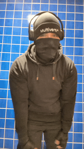 a man wearing headphones and a multiverse beanie stands in front of a blue tiled wall