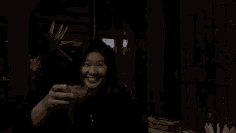 a woman is holding a drink in her hand in a dark room and smiling .
