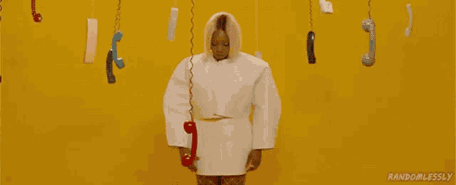 a woman in a white dress is surrounded by telephones hanging from a yellow wall .