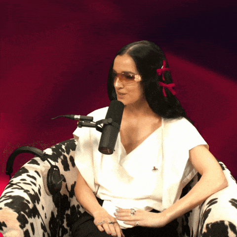 a woman wearing sunglasses sits in front of a microphone on a cow print chair