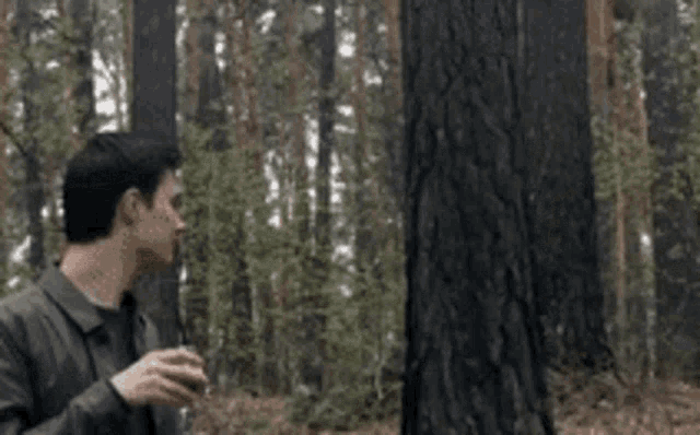 a man is standing in the woods holding a glass of wine while another man holds a sword .