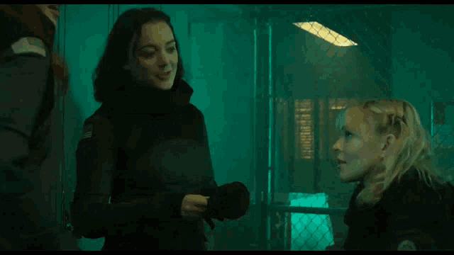 two women standing next to each other in a dark room talking