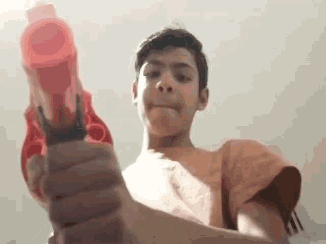 a young boy is holding a red nerf gun in his hand and pointing it at the camera .