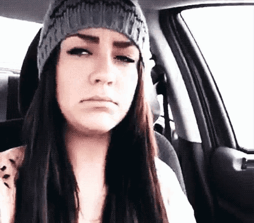 a woman wearing a beanie is sitting in the back seat of a car making a sad face .