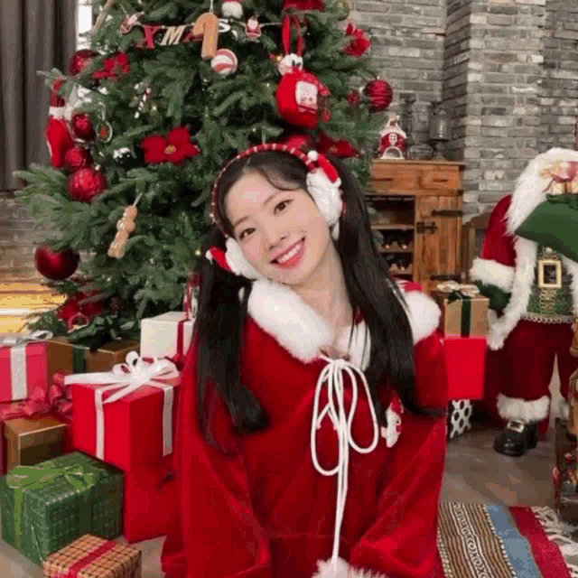 a girl in a santa claus costume is standing in front of a christmas tree and gifts .