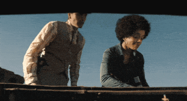 a man in a vest and a woman in a blue shirt are standing next to each other