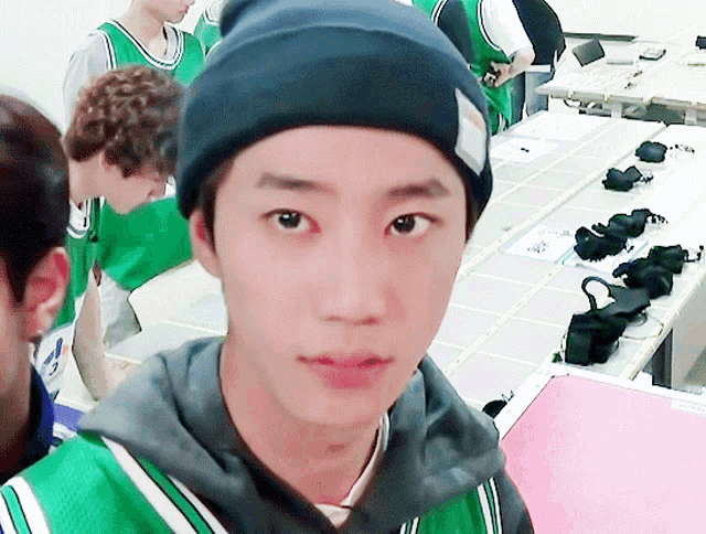 a young man wearing a black beanie and a green sweater looks at the camera