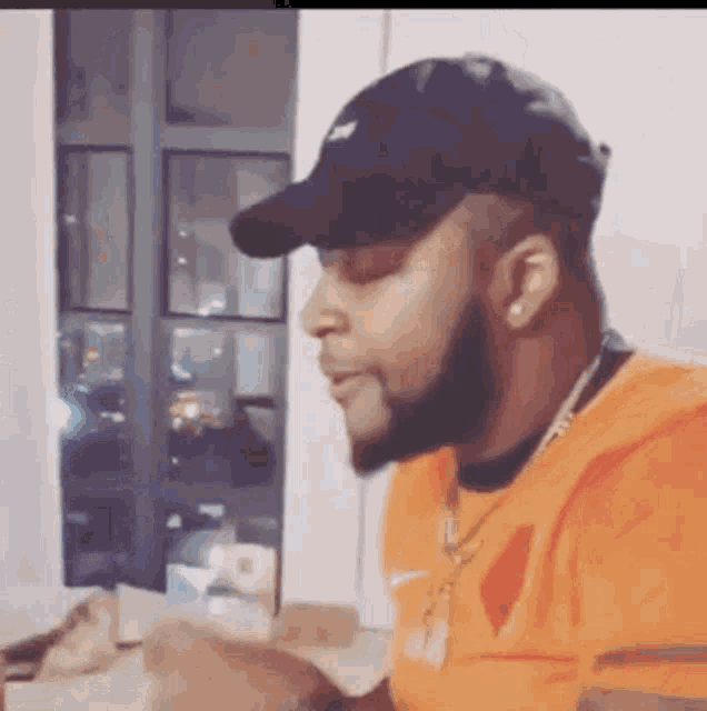 a man wearing a hat and an orange shirt is sitting at a table .