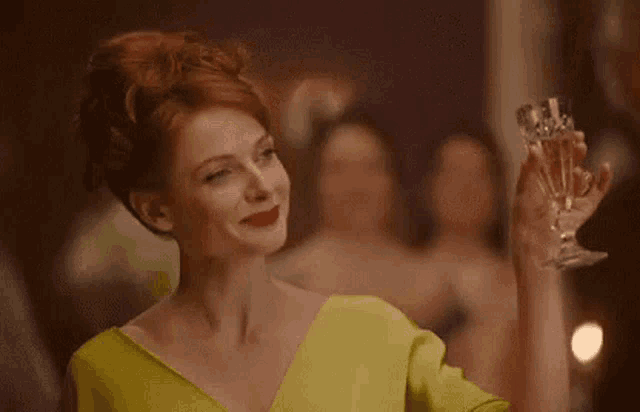 a woman in a green dress is holding a glass of champagne in her hand .