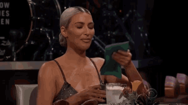 a woman in a dress is sitting at a table with a drink and looking at a piece of paper .