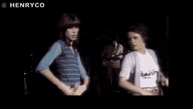 two women are standing next to each other on a stage in front of a man playing a guitar .
