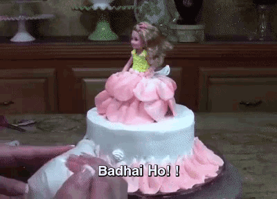 a barbie doll is sitting on top of a cake that says ' badhai ho ! '