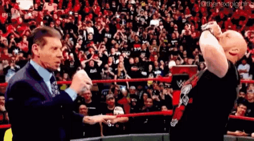 a man in a suit and tie is standing next to another man in a wrestling ring .