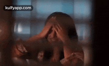a woman is covering her face with her hands behind a glass door .