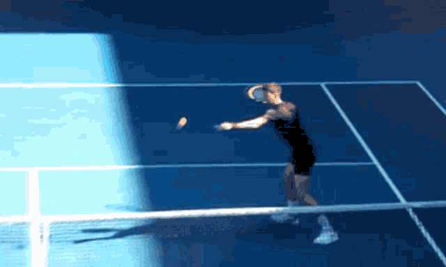 a man in a black shirt is hitting a tennis ball on a blue court