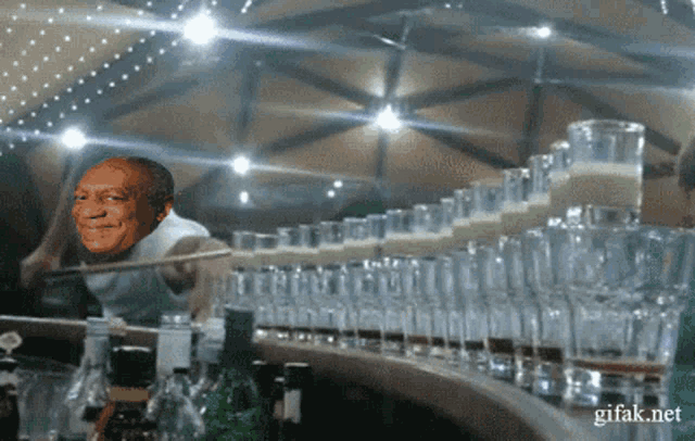 a gif of bill cosby behind a bar full of glasses