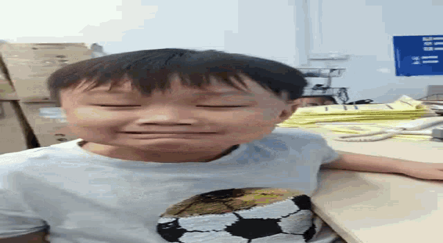 a young boy with a soccer ball on his shirt is crying while sitting at a desk .