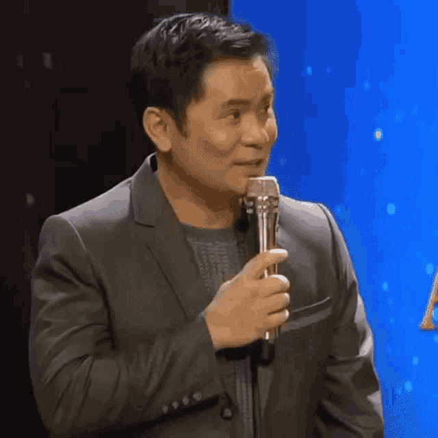 a man in a suit is holding a microphone in his hand and smiling .