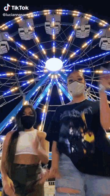 two girls wearing face masks are posing in front of a ferris wheel