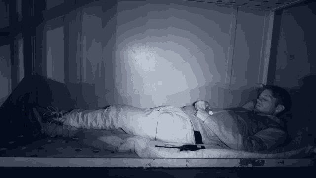 a man is laying on a mattress in a dark room with his legs crossed