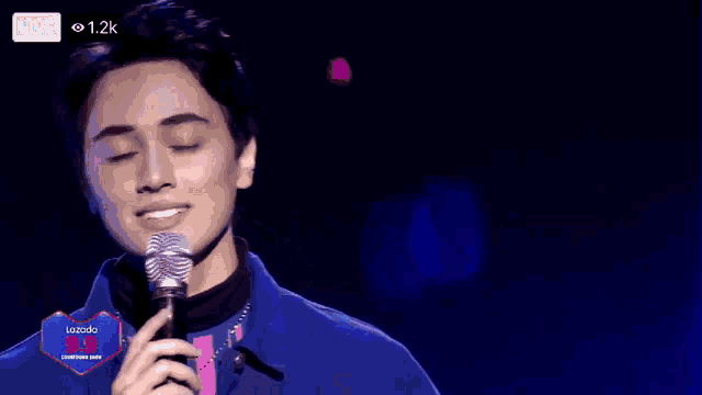 a young man is singing into a microphone on a stage with a live 1.2k button in the corner