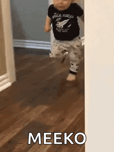 a baby is walking across a wooden floor with the word meeko written on it .
