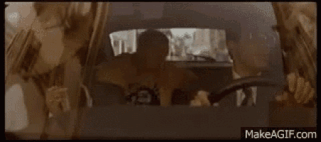 a man in a suit is driving a car and holding a newspaper in his hand .