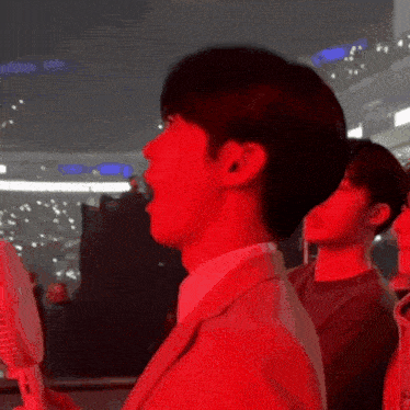 a man in a suit is standing in a dark room with a red light behind him
