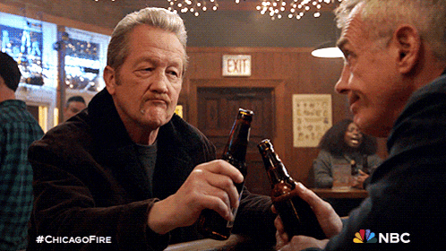 two men toasting with beer bottles in front of an exit sign on a wall