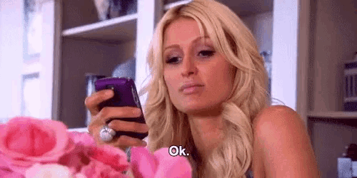 a blonde woman is holding a cell phone and saying ok .