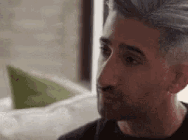 a man with gray hair is sitting in front of a window looking out .