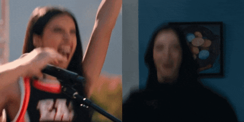 a cheerleader is screaming into a microphone and another cheerleader is smiling in front of a microphone .