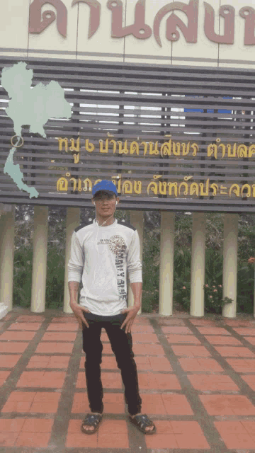 a man in a blue hat stands in front of a sign that says ' thailand ' on it