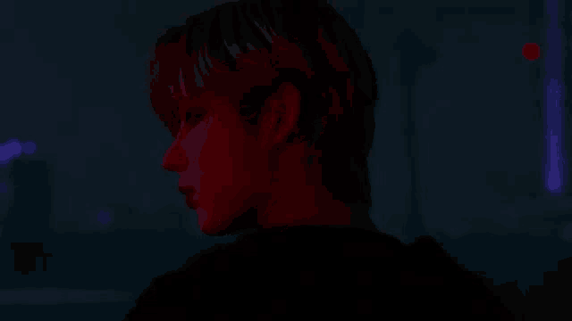 a close up of a man 's face in a dark room with a red light behind him .